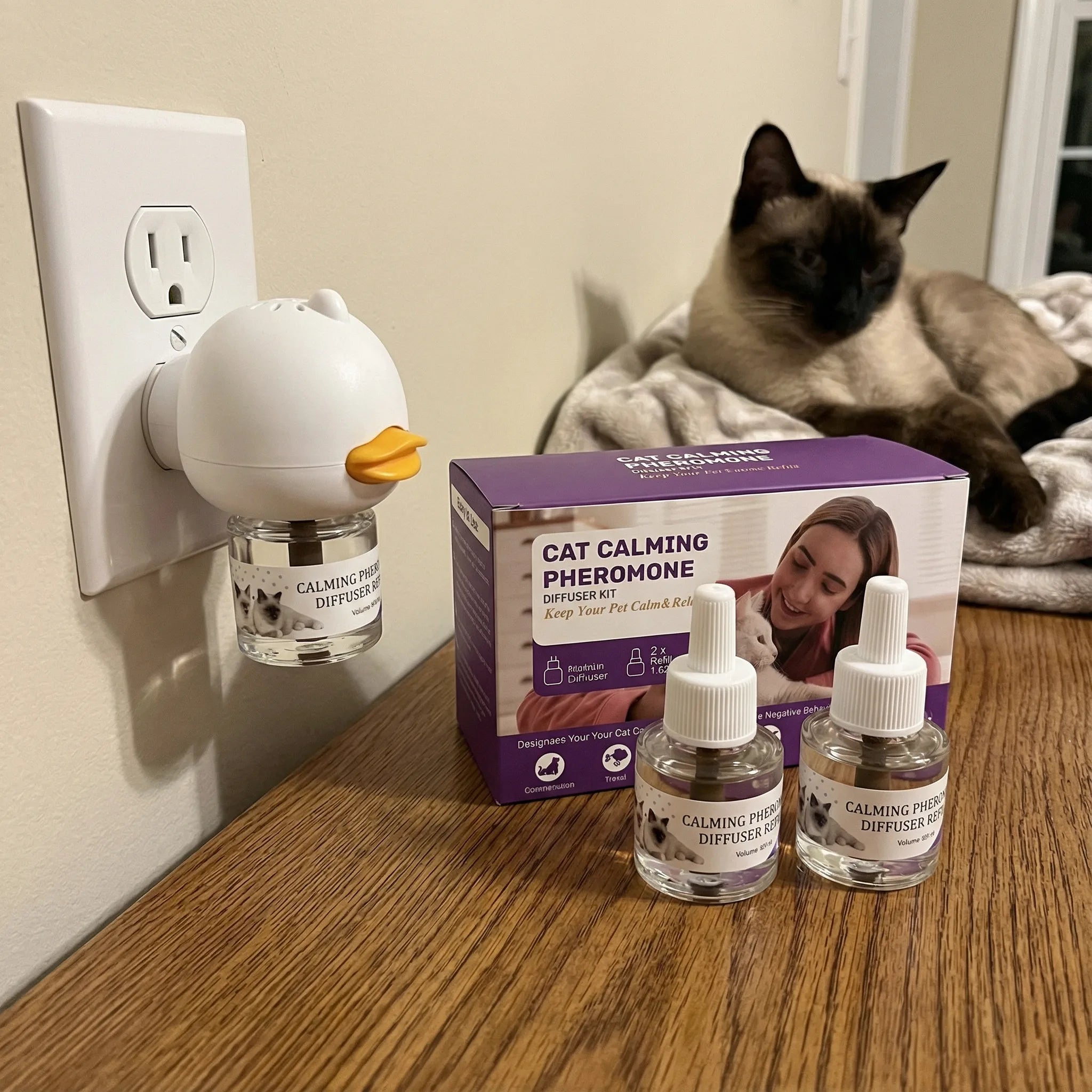 AromaPaw diffuser plugged in with box and refills, Siamese cat relaxing nearby